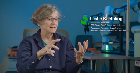 Prof. Leslie Kaelbling mid-conversation in front of a table with robotics displayed