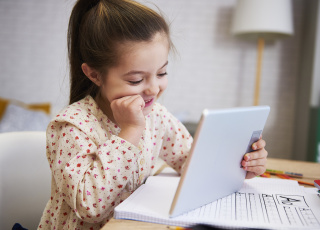 girl using a tablet while completing a worksheet on the alphabet